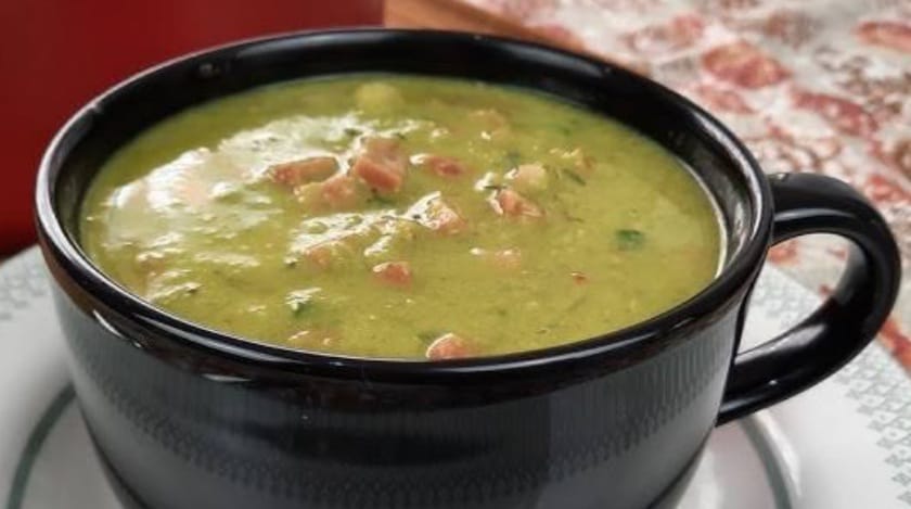 Caldo verde servido em caneca preta sobre prato branco